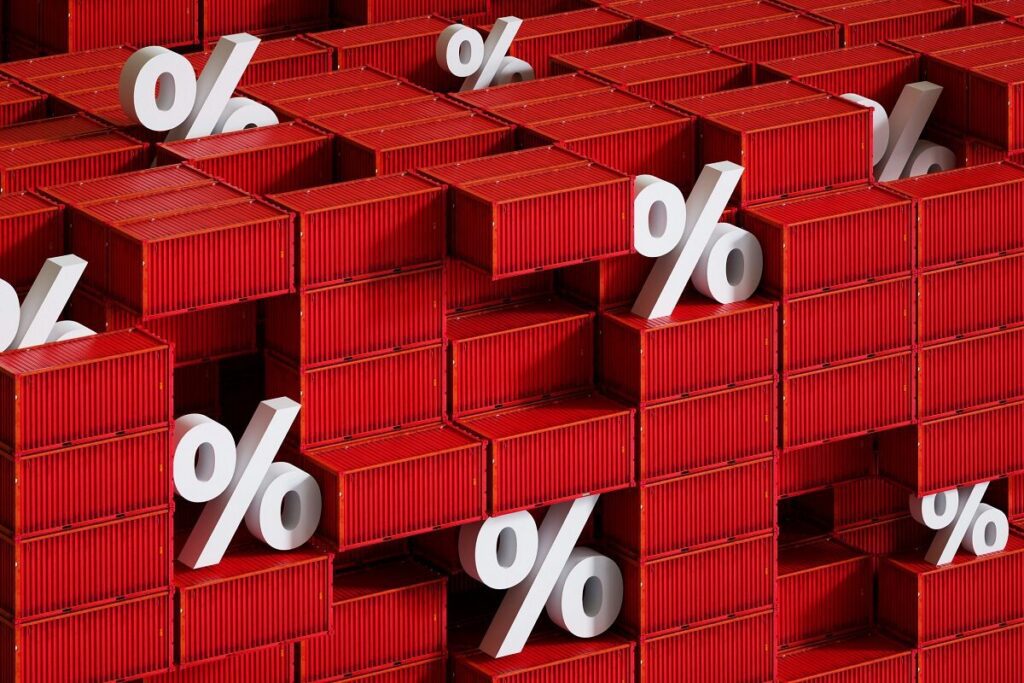 A 3D conceptual image of a dense wall of stacked red shipping containers. Several large, white percentage symbols are interspersed and protruding among the corrugated boxes, visually representing international trade tariffs, freight rate percentages, or global commerce metrics.