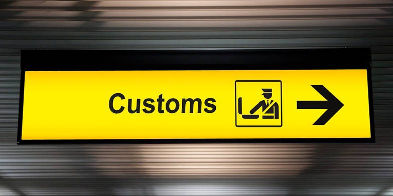 UKCA and UK Customs Compliance: Product Regulations 3 A yellow sign reading "Customs" with a customs officer icon and a right-pointing arrow, mounted on a metal wall.