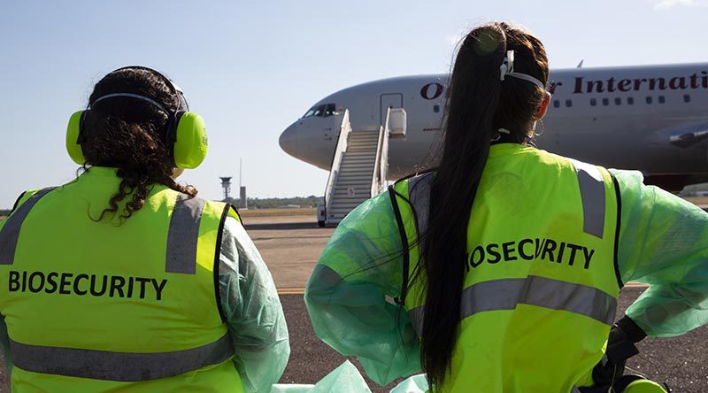 Australia Multi-Carrier Shipping: Cost Control for Alibaba Imports 3 Two biosecurity officers in high-visibility vests and protective gear standing on an airport tarmac, facing a white international airplane, representing border biosecurity controls.