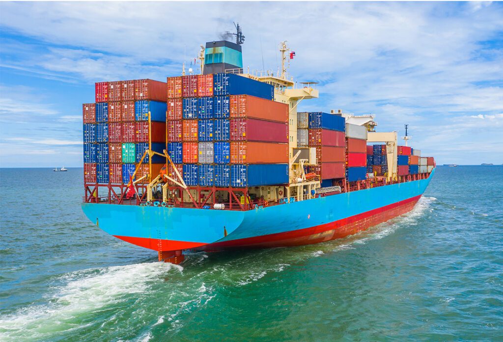 A large blue container ship loaded with colorful shipping containers sailing through the ocean under a clear sky, representing global Sea Freight.