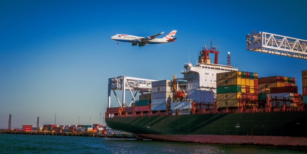 Australia Shipping Modes: Sea vs Air with AUD 1,000 Threshold 2 A large green container ship docked at a port with a British Airways plane flying overhead, illustrating global logistics and Sea & Sea Freight.