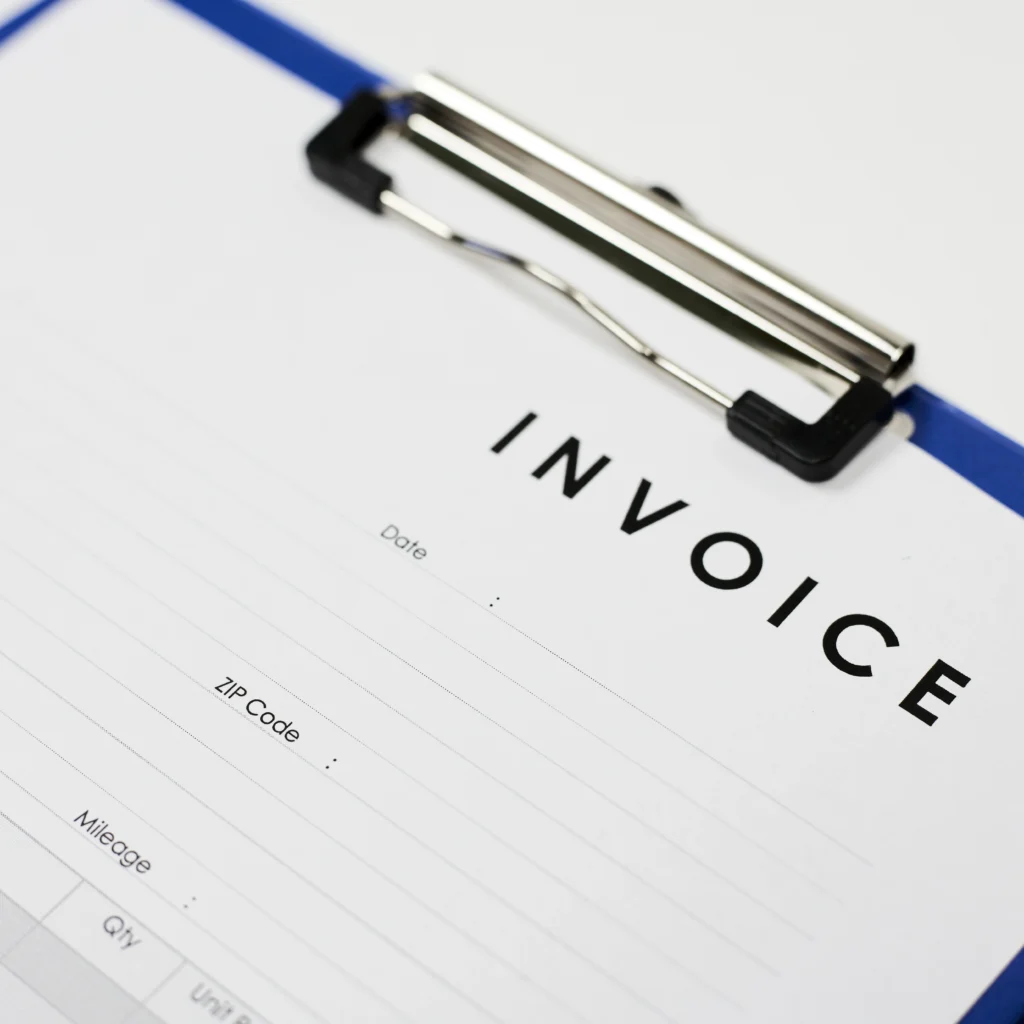 A close-up image of a blank commercial invoice form on a blue clipboard. Featuring fields for shipping details, dates, and quantities, the document represents the essential paperwork required for international trade, customs clearance, and order processing.